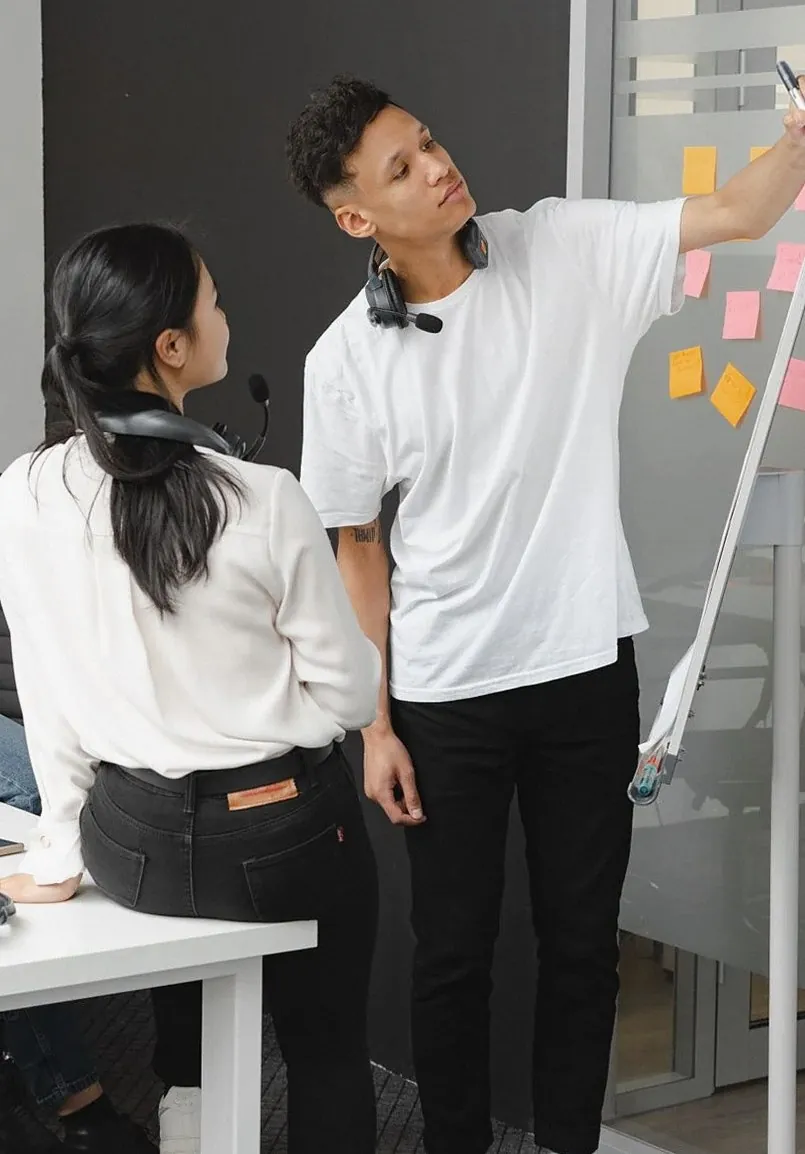 付箋を貼ったボードの前で話し合う二人（イメージ写真）